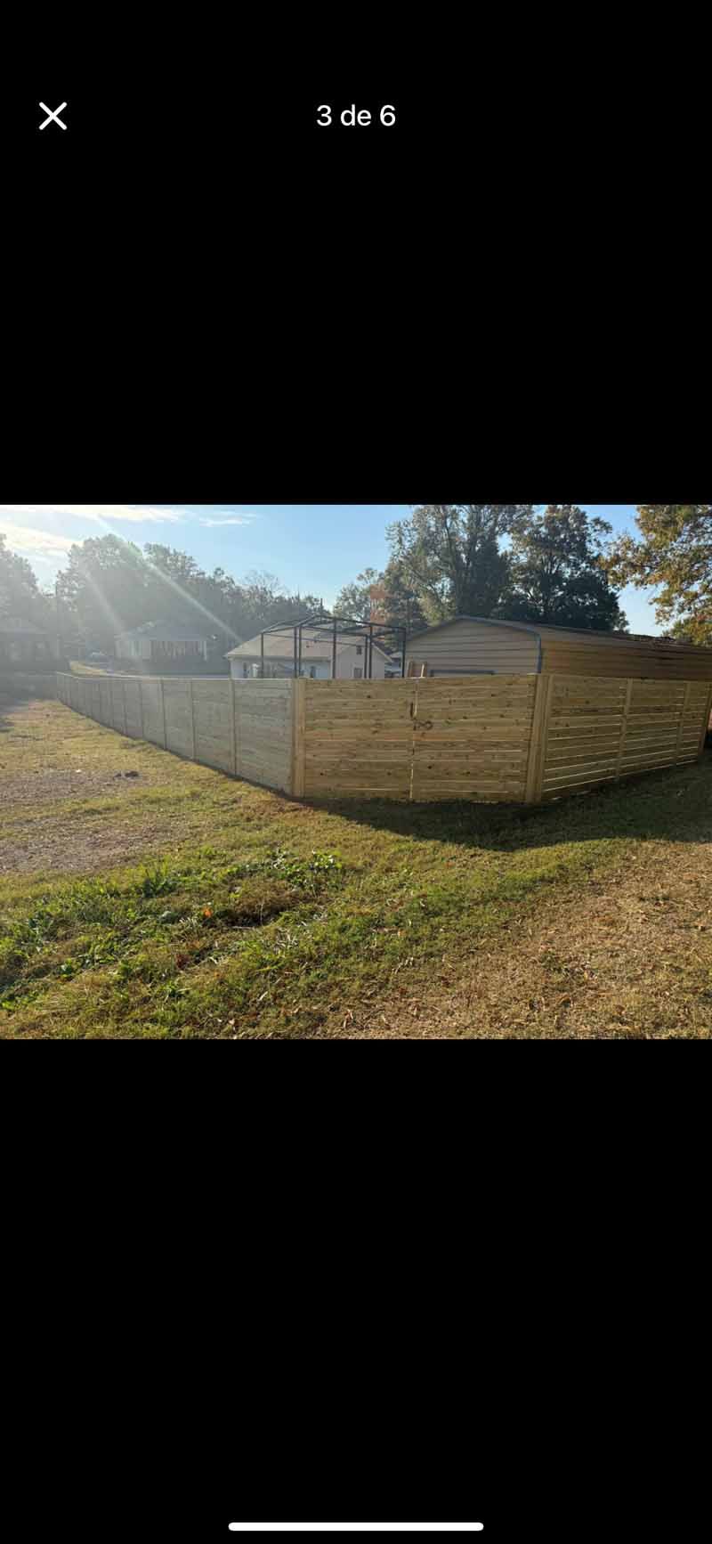 Backyard with a tan privacy fence, grassy yard, and trees in bright sunlight.