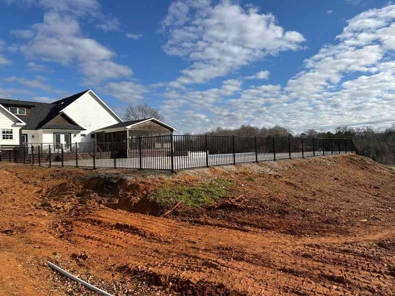 New house beside a fenced, muddy construction lot under a cloudy blue sky
