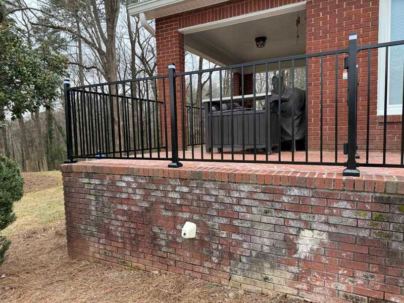 Brick patio with black metal railing and covered porch beside a brick house.