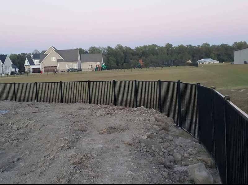 Flooded construction site with a black silt fence, muddy ground, and houses in the distance
