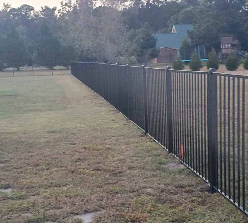 Long black metal fence along a grassy yard beside houses at dusk