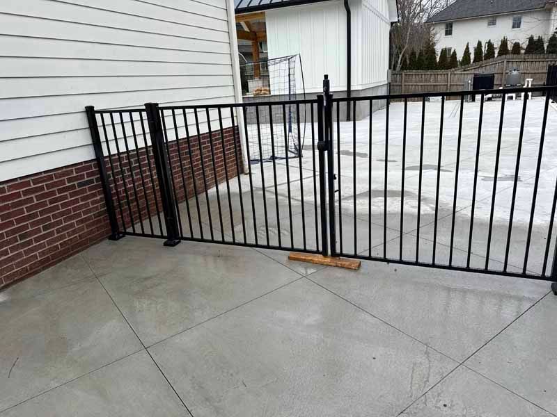 Black metal gate blocking a snowy driveway beside a brick-and-siding house