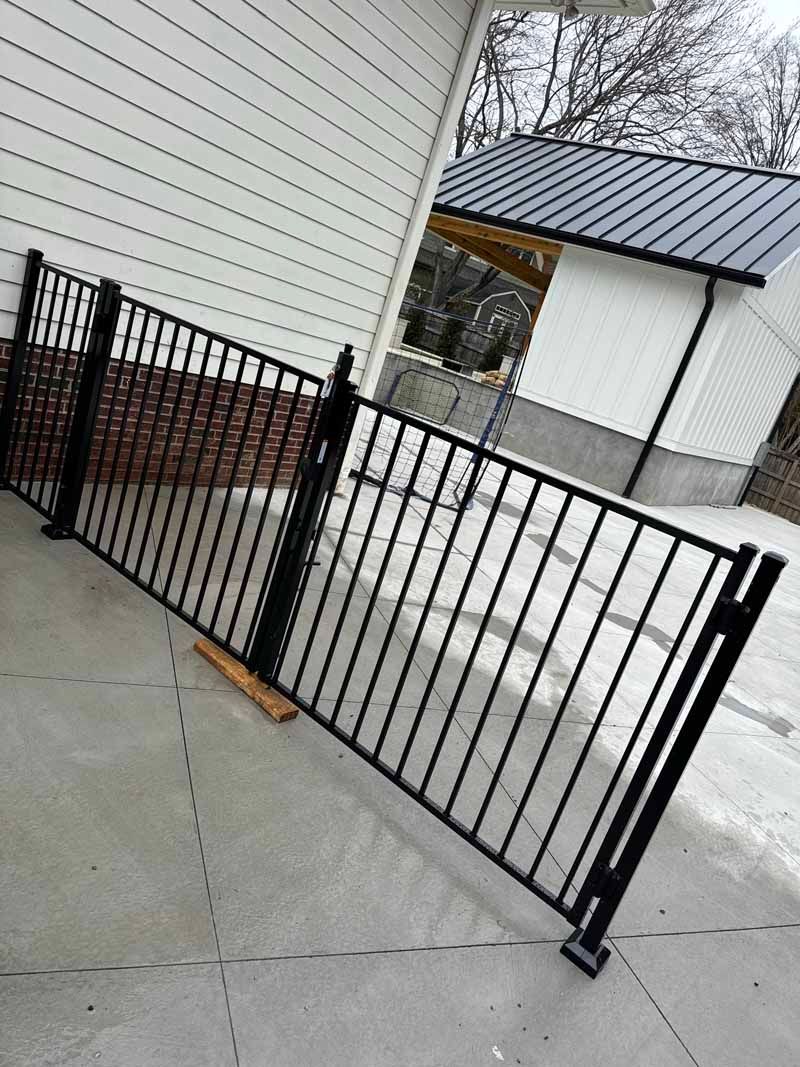 Black metal fence blocking a sloped concrete driveway beside a white house and detached garage