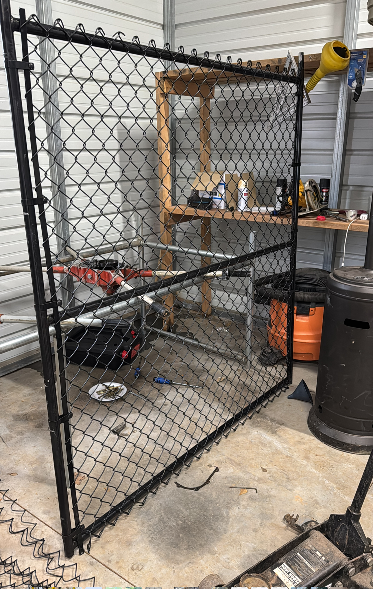 Outdoor chain-link gate by a workshop shelf, with tools and equipment stored behind it.