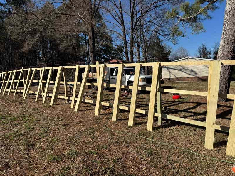 Long row of pale wooden fence panels leaning along a grassy roadside under blue sky