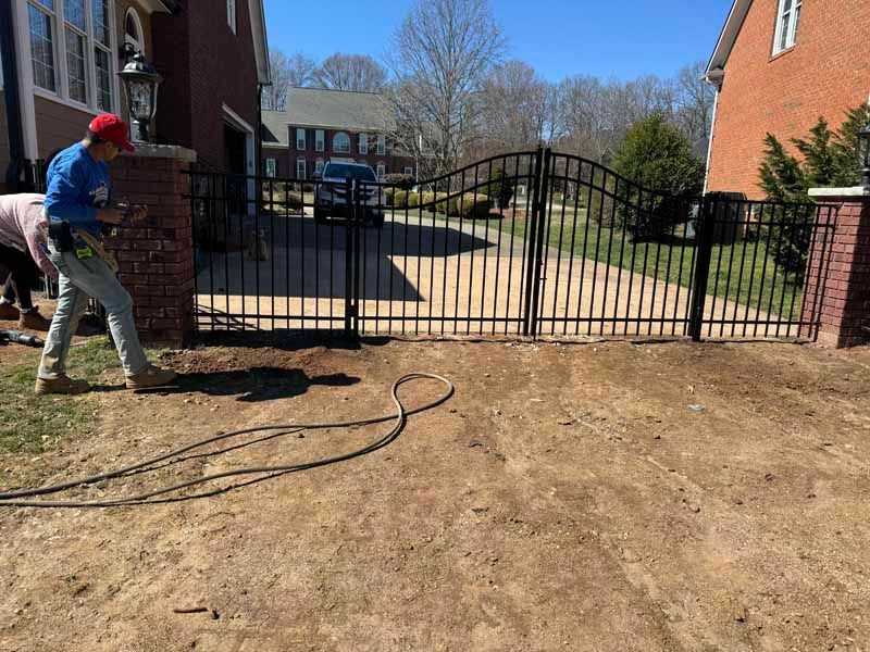 Worker spraying concrete beside a black metal gate between apartment buildings