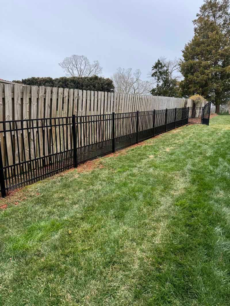 Wooden fence with black metal railing along a green grassy yard under a cloudy sky