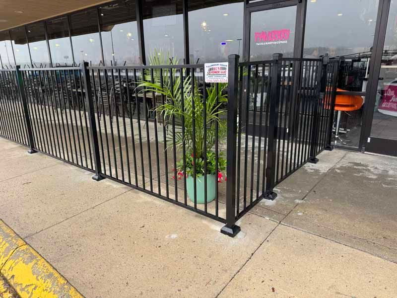 Black metal patio fence and potted plant outside a storefront with large glass windows