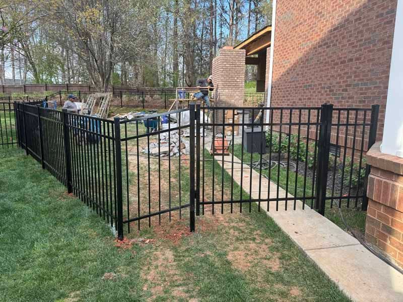 Black metal fence along a grassy walkway beside a brick building and patio area