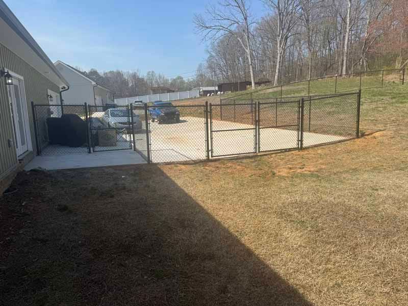 Backyard with chain-link fence, concrete patio, parked car, and house beside a brown lawn