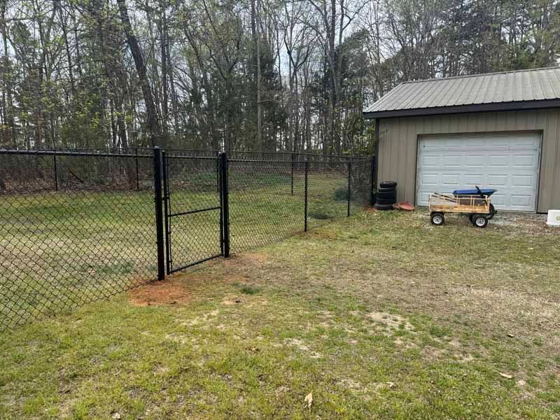Chain-link fence along a yard beside a gray garage and grassy backyard.
