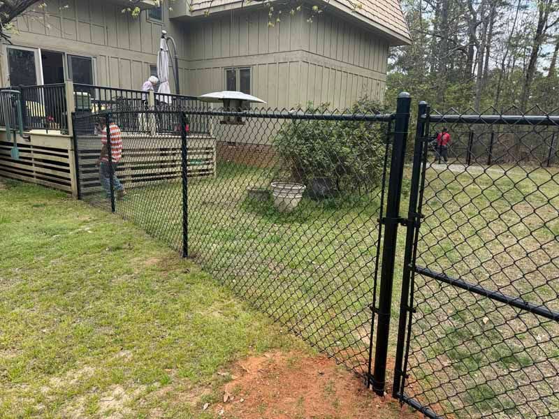 Backyard chain-link gate in front of a house with grass and a small patio umbrella