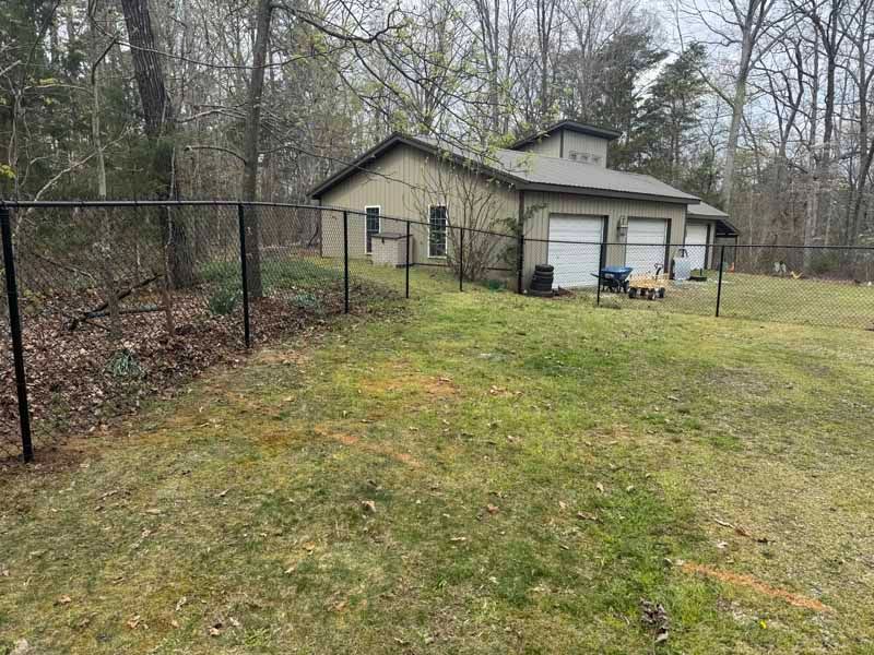Backyard with a small beige shed/garage, chain-link fence, and leaf-covered woods in the background