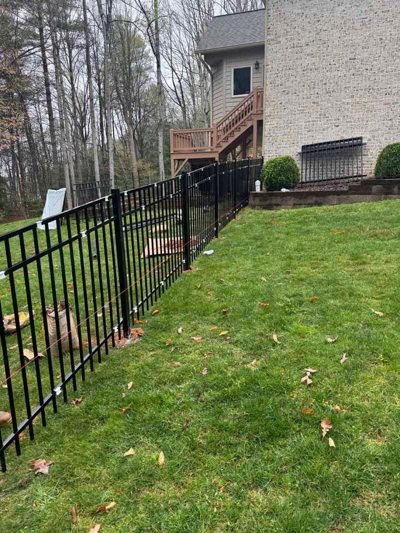 Black metal fence beside a grassy yard leading to a house with stairs and a small deck