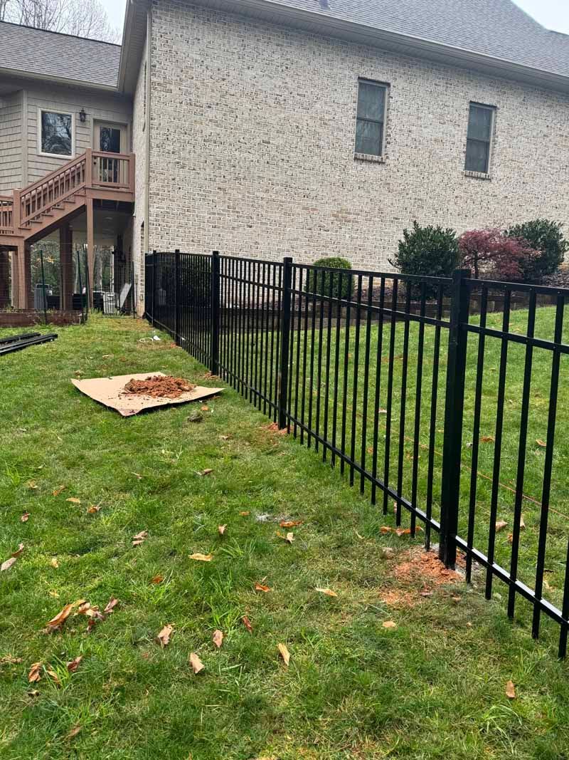 Black metal fence along grassy yard beside a stone house and wooden stairs