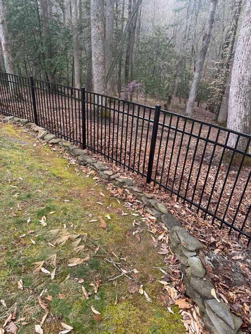 Black metal fence along a wooded, leaf-covered slope on a foggy day