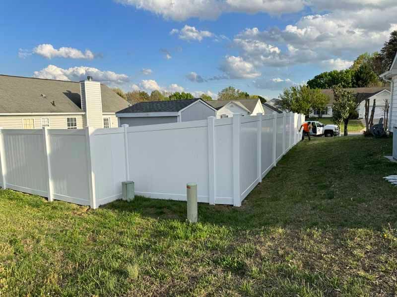 White vinyl fence surrounding a backyard beside houses under a partly cloudy sky