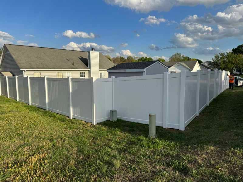 White vinyl privacy fence around a corner yard beside a house under a blue sky