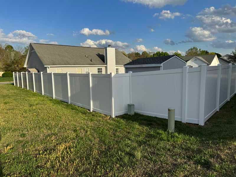 White vinyl fence around a grassy yard beside a suburban house under a blue sky.