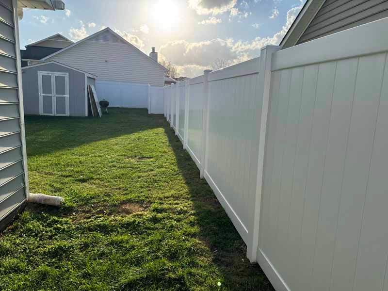 Backyard with green grass, white vinyl fence, and a small shed in bright sunlight
