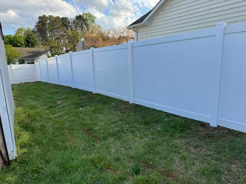Long white vinyl fence along a grassy yard beside a house