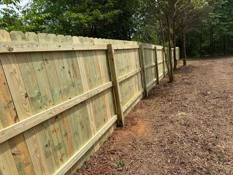 Wooden privacy fence along a wooded dirt path
