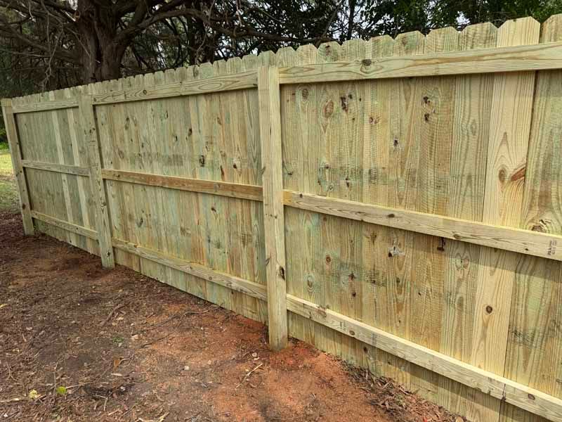 Wooden privacy fence along a dirt path, with trees visible behind it.