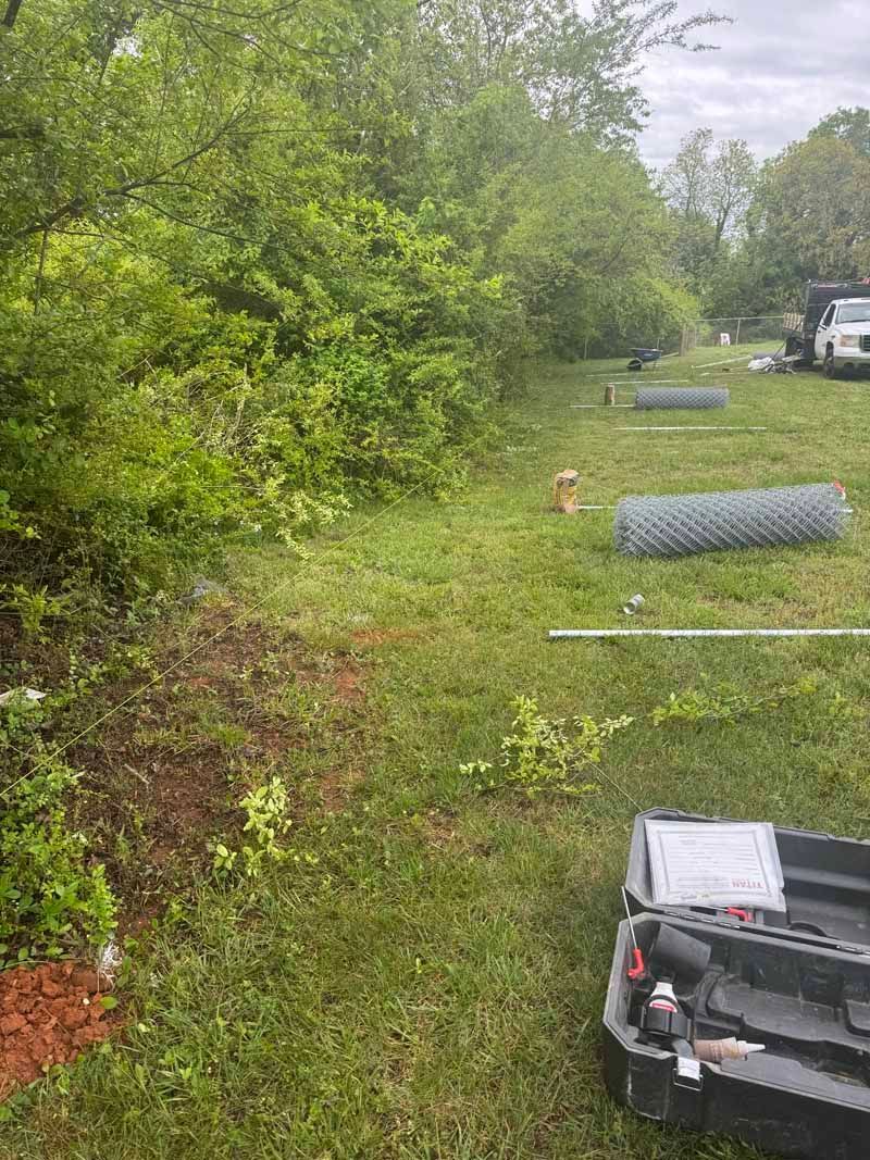 Outdoor grassy roadside with trees, a rolled wire fence section, and a black truck in the foreground.