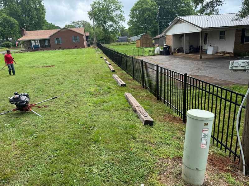 Backyard with newly cut grass, fence line, and a person using a lawn mower near a house