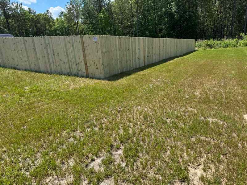 Wooden privacy fence beside a grassy field under a clear blue sky.