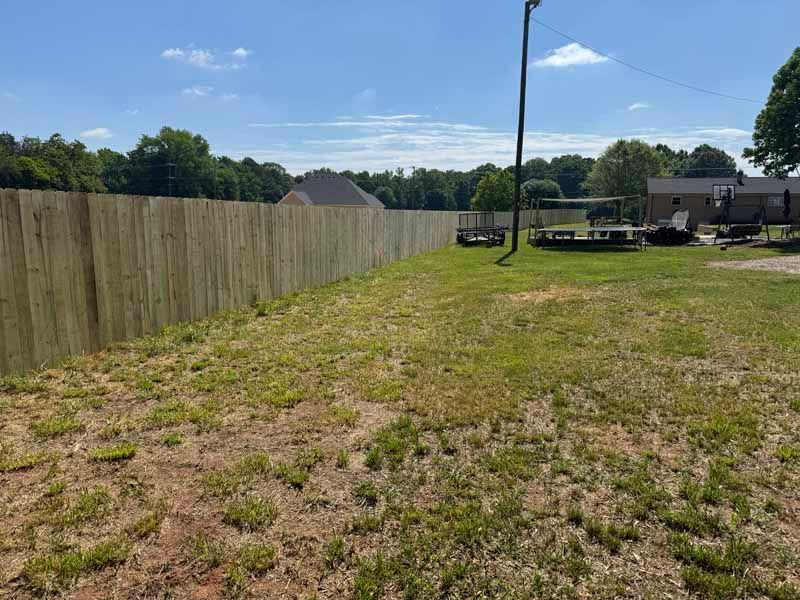 Grassy backyard with a wooden fence, clear blue sky, and a trampoline near a house