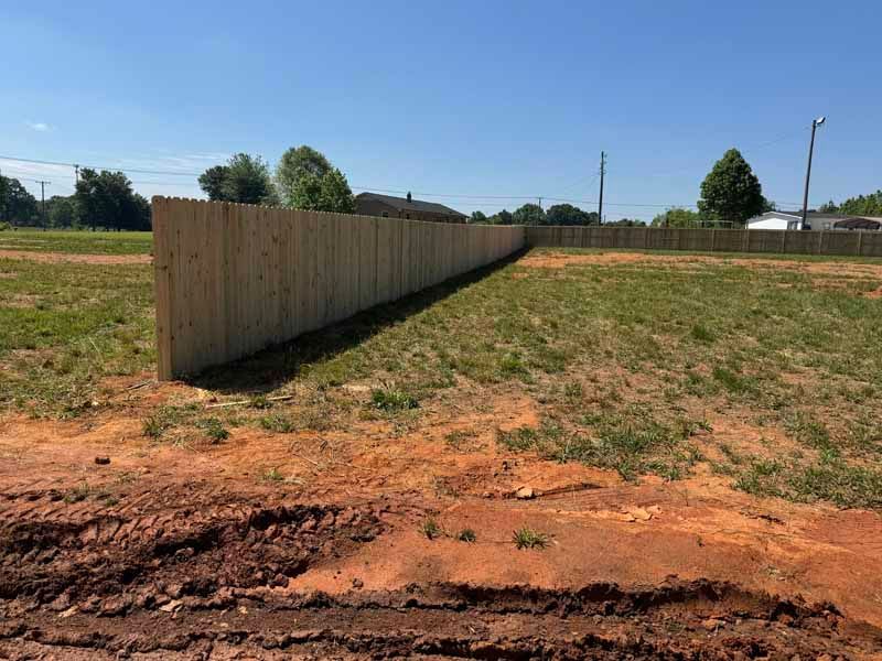 Long wooden privacy fence along a dry grassy lot under a clear blue sky
