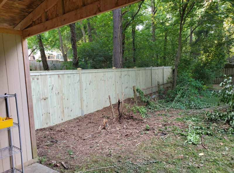 Backyard with a new wooden fence, dirt ground, and trees beyond the yard