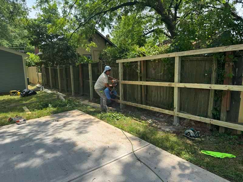 Worker installing a wooden fence beside a driveway in a leafy backyard