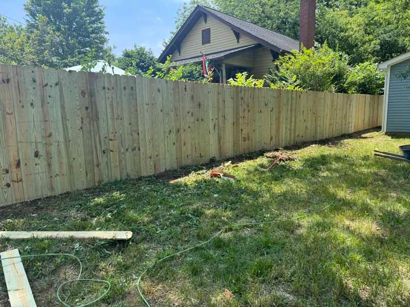Backyard with a long wooden privacy fence and grassy lawn, house and shed in the background.
