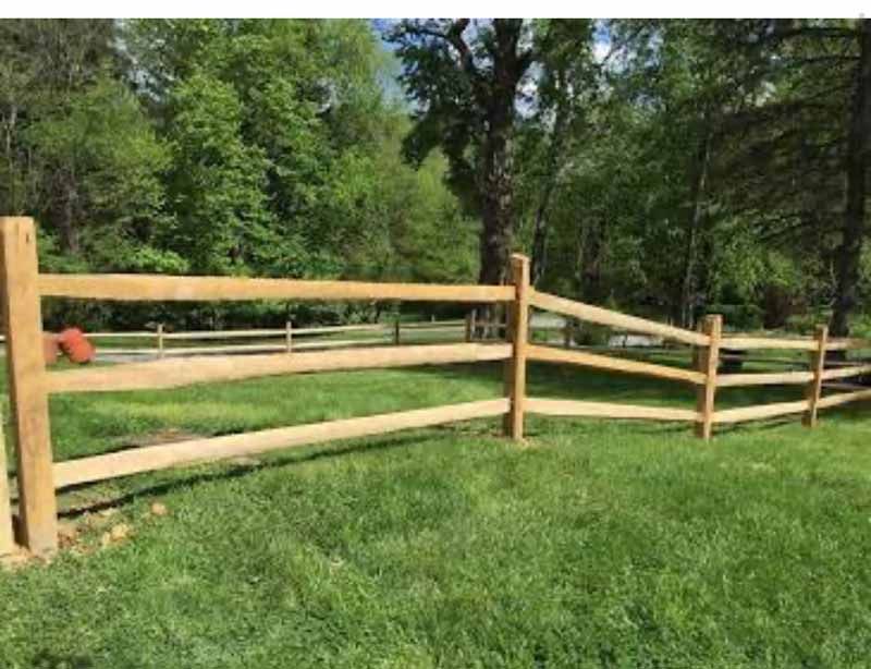 Wooden split-rail fence along a grassy yard with trees in the background
