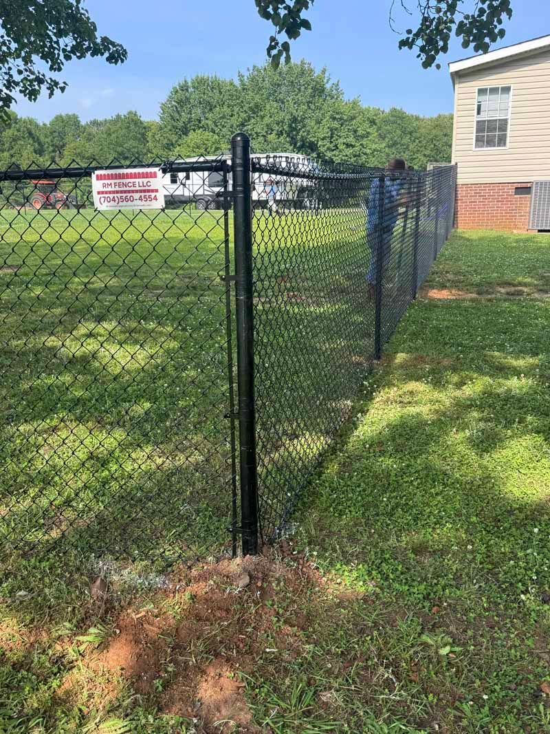 Black chain-link fence corner beside a beige building and grassy yard on a sunny day
