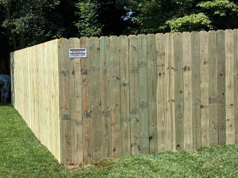 Wooden privacy fence corner in a grassy yard, with a small posted sign near the top.