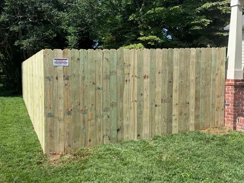 Wooden privacy fence beside a grassy yard, with trees and a brick corner visible.