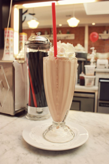 Chocolate milkshake with whipped cream, red straw, diner setting.