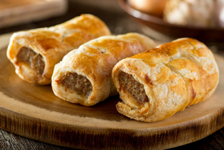 Three golden-brown sausage rolls on a wooden cutting board.