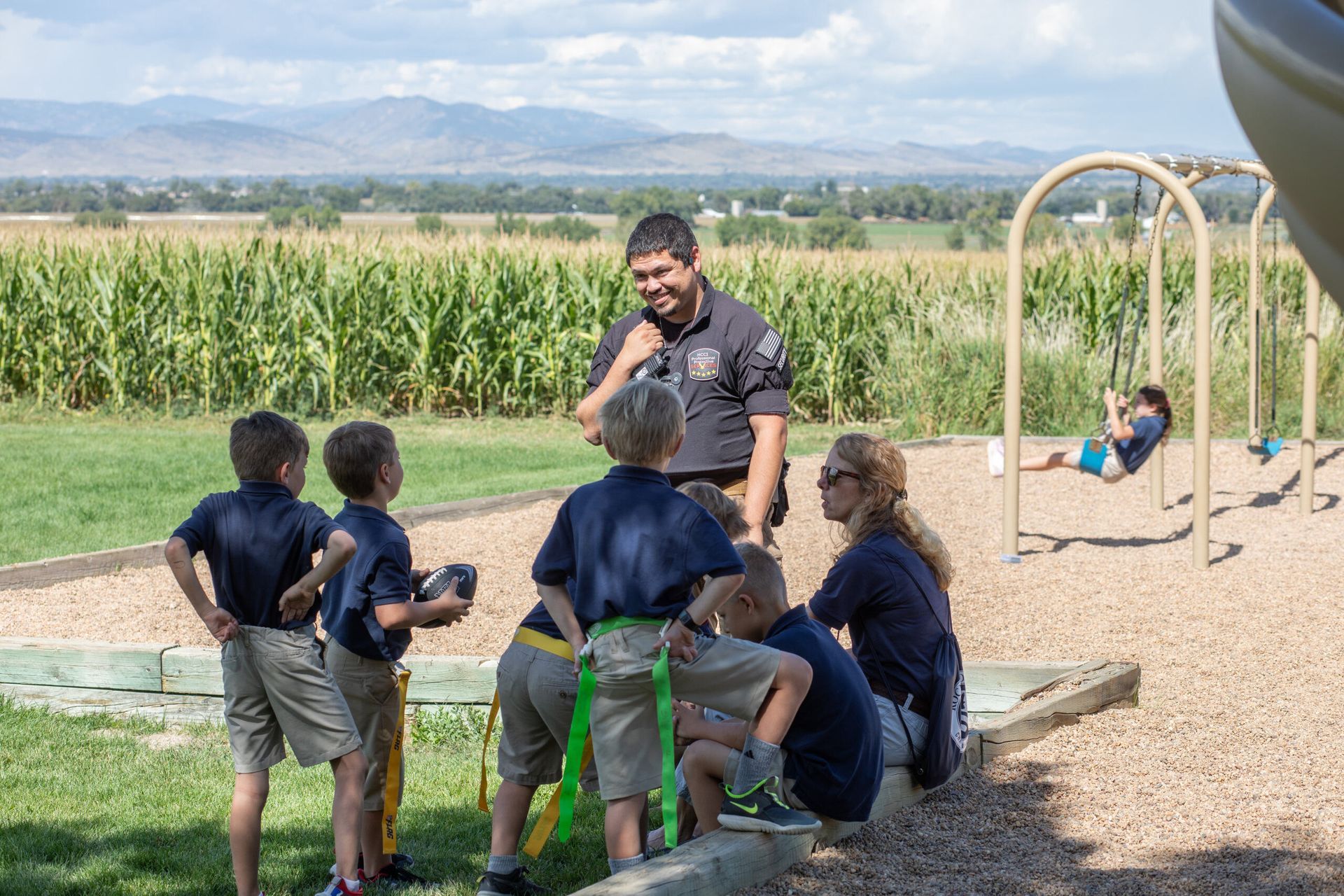 A group of children are standing around a playground with a police officer.