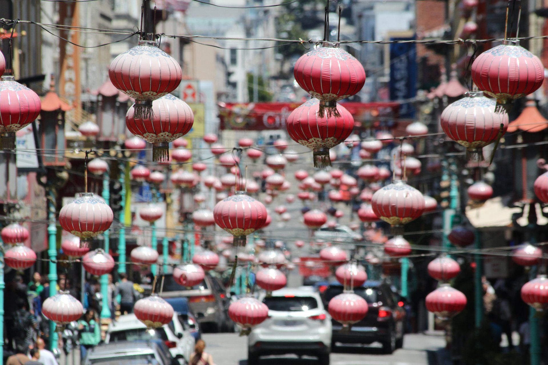 A busy street with lots of red lanterns hanging from a pole.
