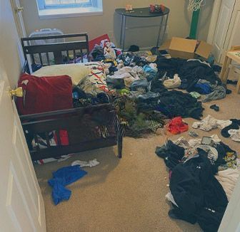A bedroom with a bed and a lot of clothes on the floor.