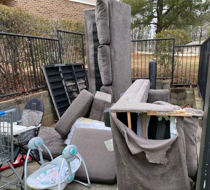 A pile of furniture is sitting on the ground in front of a fence.