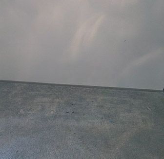 A concrete floor with a white wall in the background and a rainbow in the sky.