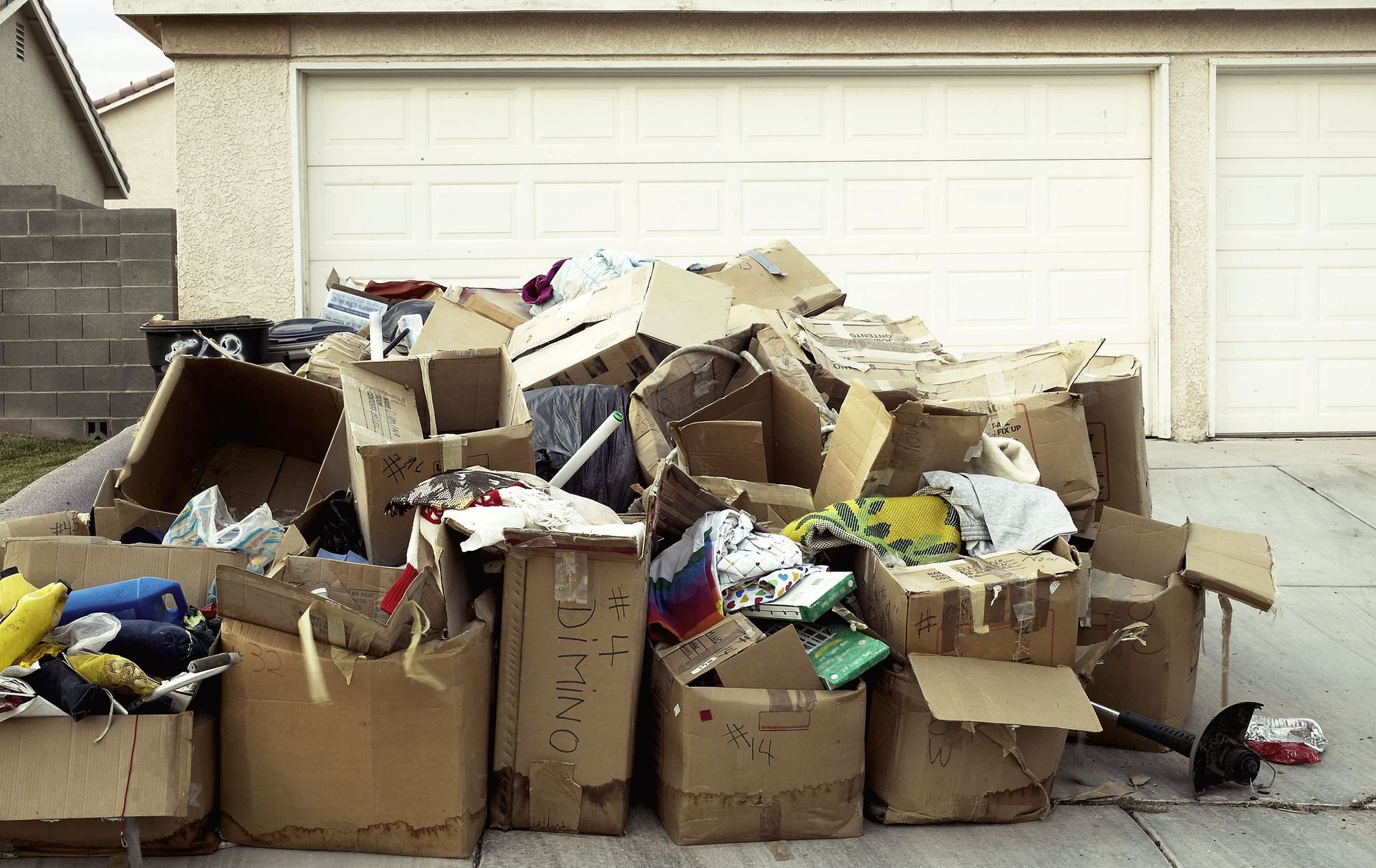 Overflowing boxes and trash piled in a driveway in front of a white garage door