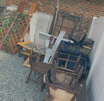 A pile of wooden chairs , tables , and other furniture in front of a brick building.