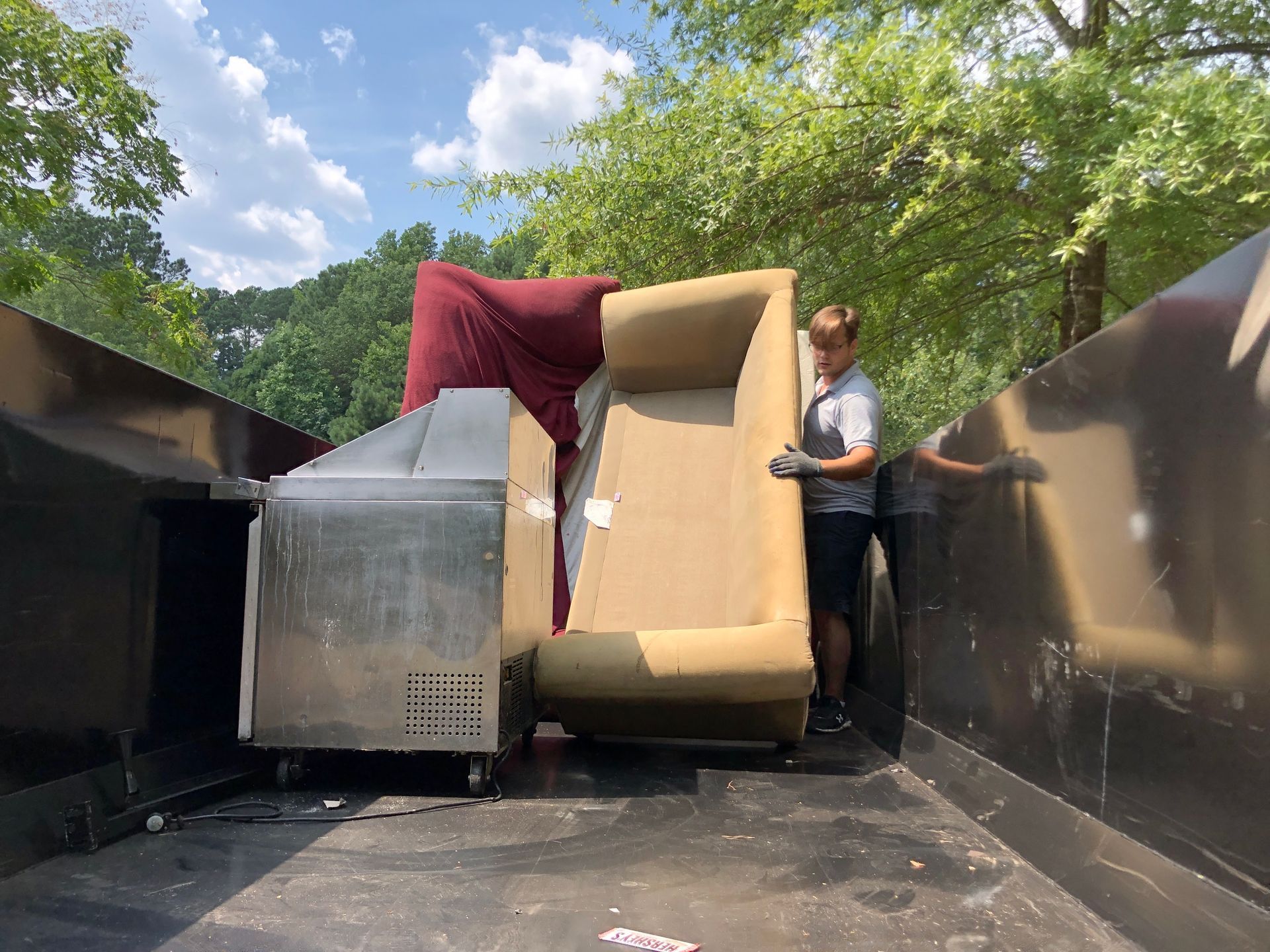 A man is loading a couch into a dumpster.