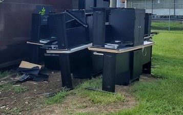 A bunch of computer desks are sitting on top of each other in the grass.